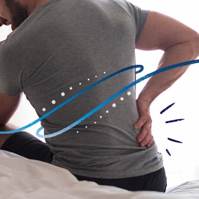 Someone sat up in bed holding one hand on the bottom of their back in pain