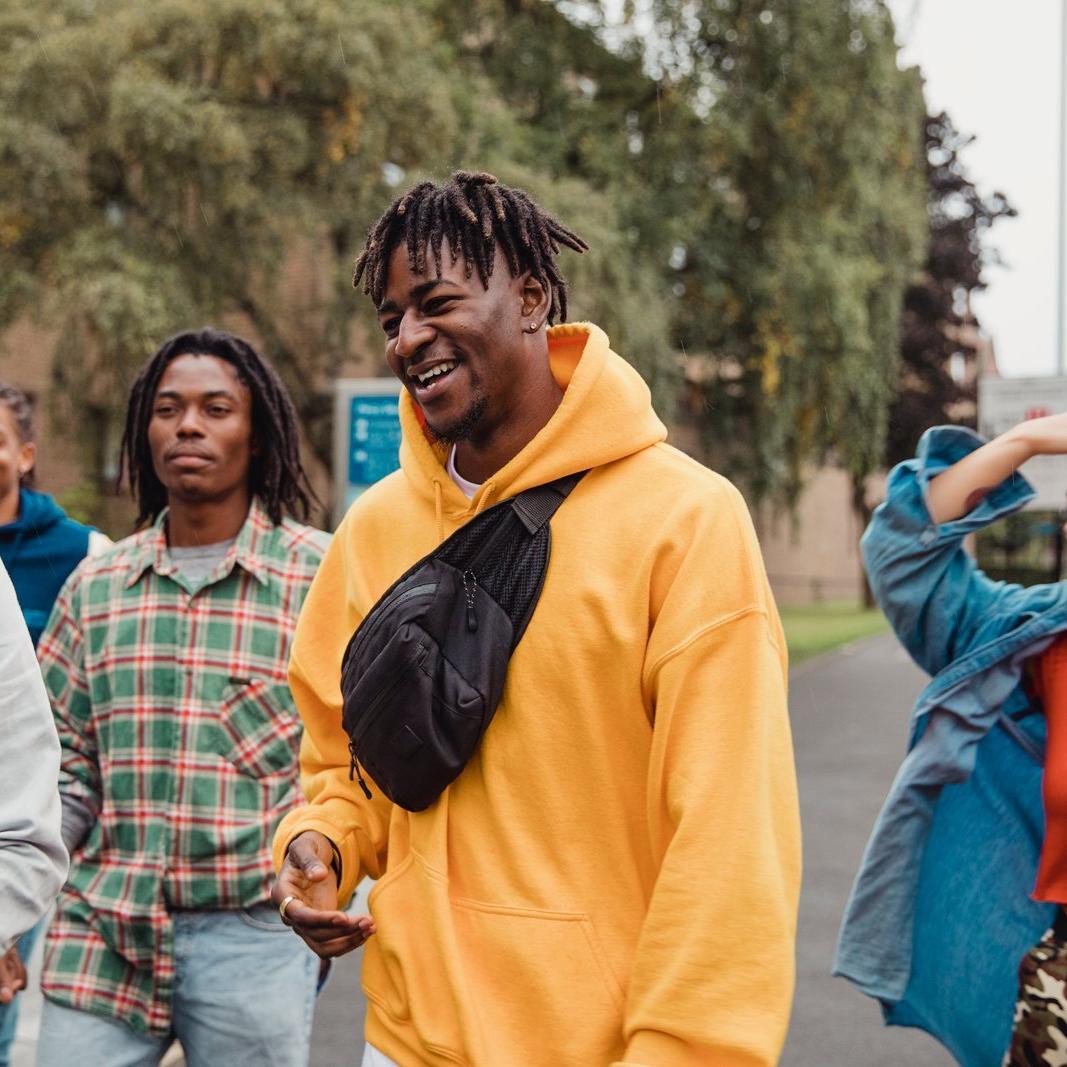 A group of young adults walking outdoors, with one wearing a yellow hoodie