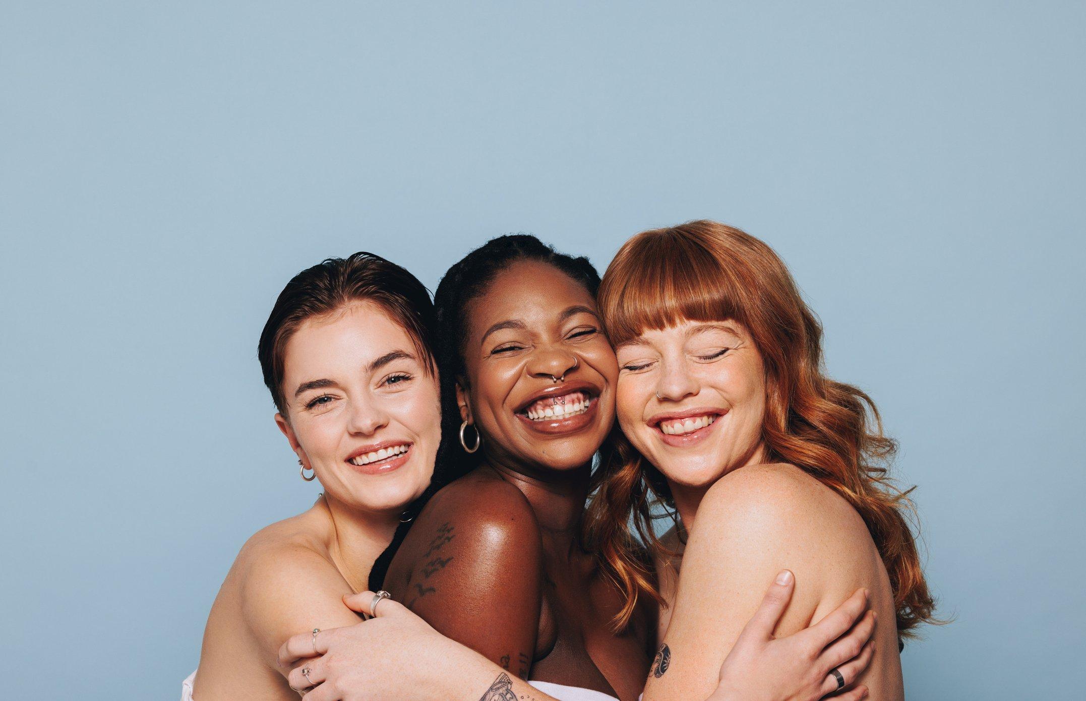 Three people hugging and smiling against a light blue background.