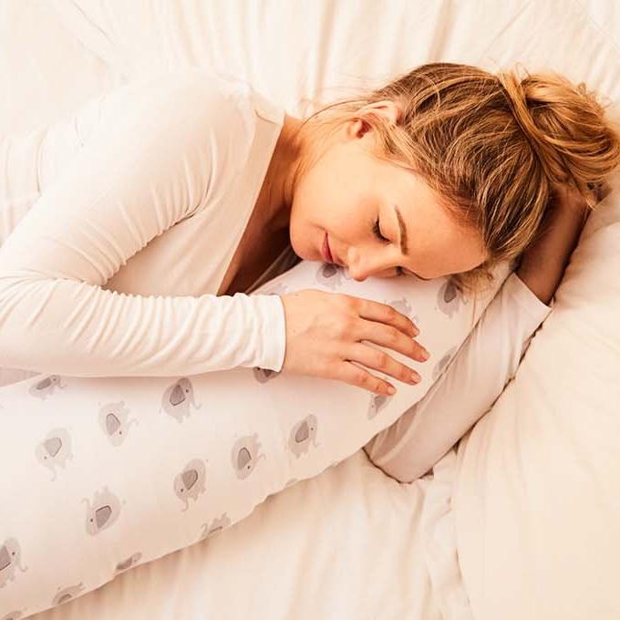 A pregnant woman asleep on her side with a pregnancy pillow