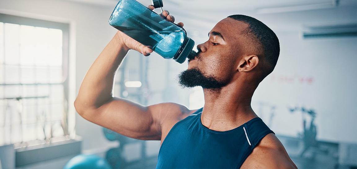 A man in a blue athletic shirt drinking from a blue water bottle in a gym