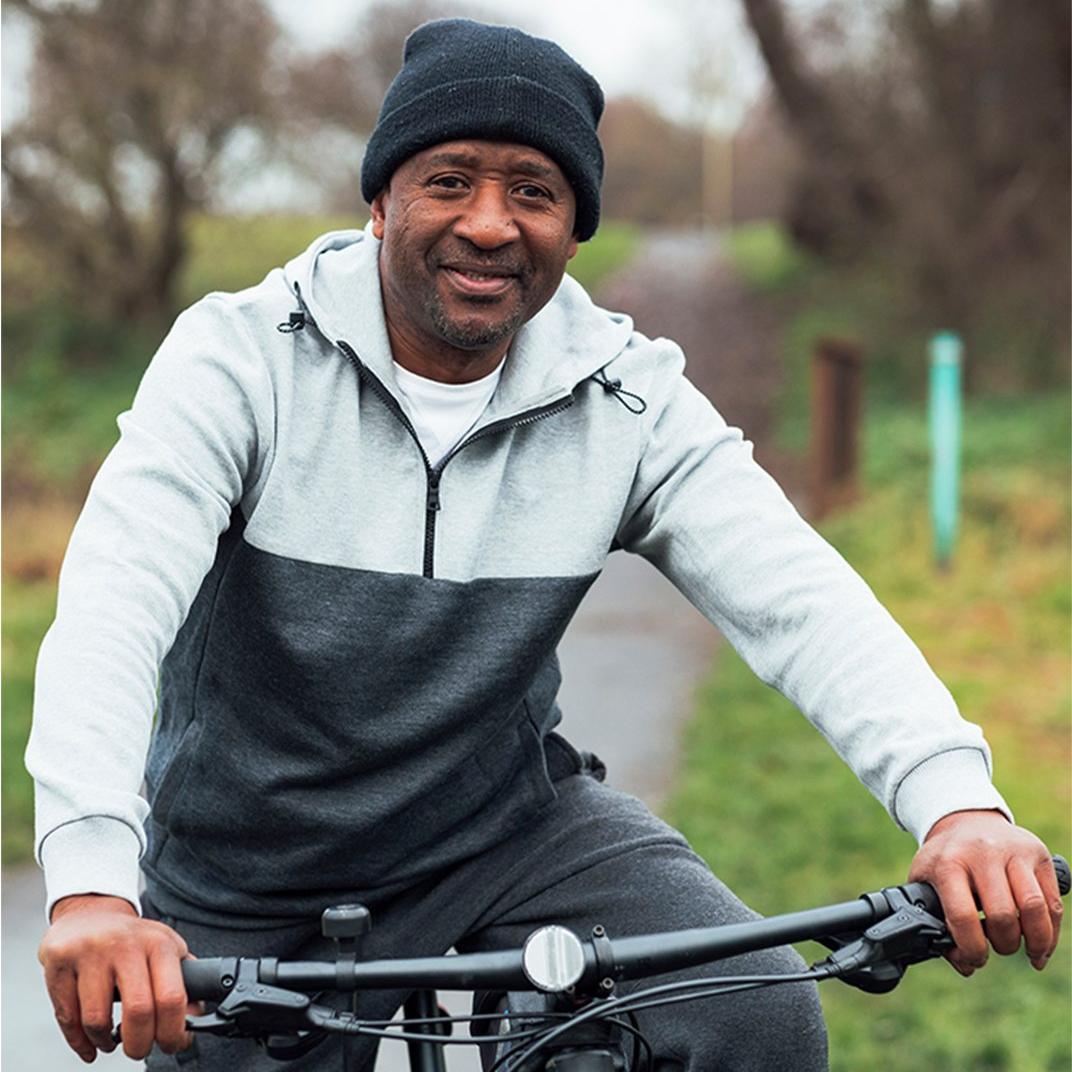 A man wearing a beanie and a two-toned grey hoodie sat on a bike outside