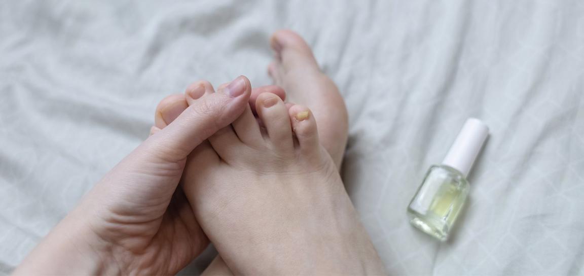 Close-up of a hand holding toes on a bed with a nail polish bottle nearby.