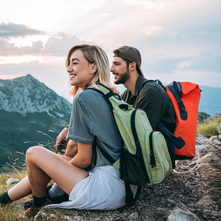 Two people with backpacks sitting down, overlooking some mountains