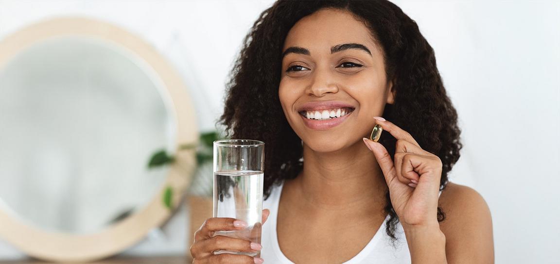 A person smiling while holding a glass of water and a pill.