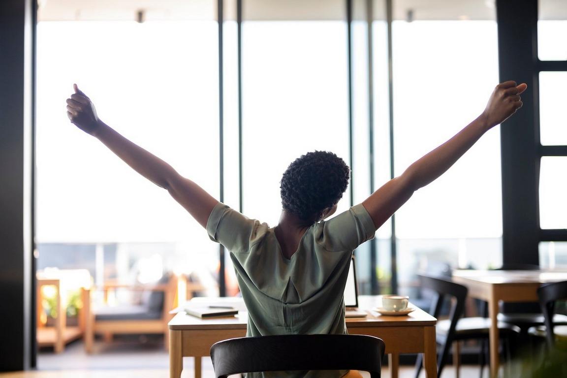 Person stretching at a table in a bright room with large windows
