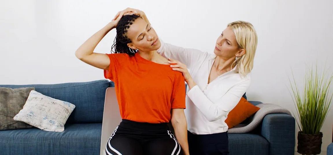 A woman stretching her neck with help from another person