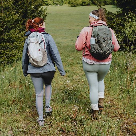 2 women wearing backpacks walking through a field