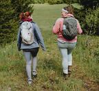 2 women wearing backpacks walking through a field