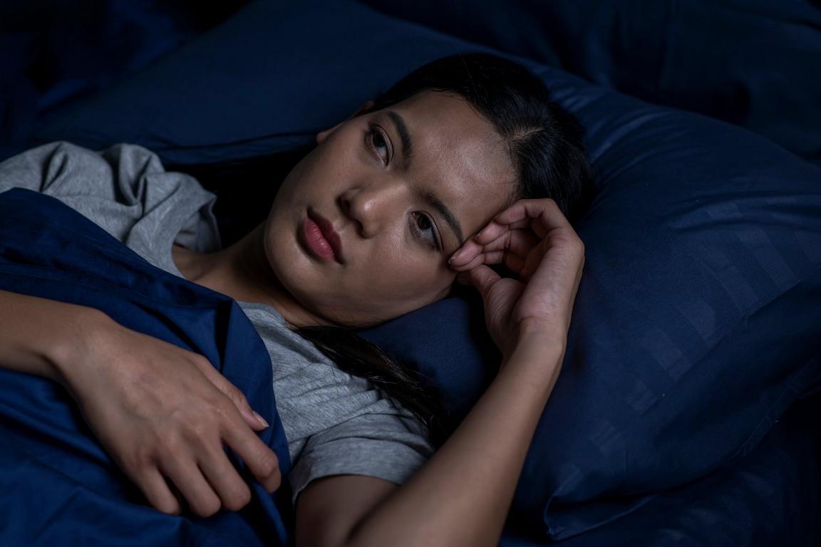 Person lying in bed, resting on a blue pillow with a thoughtful expression.