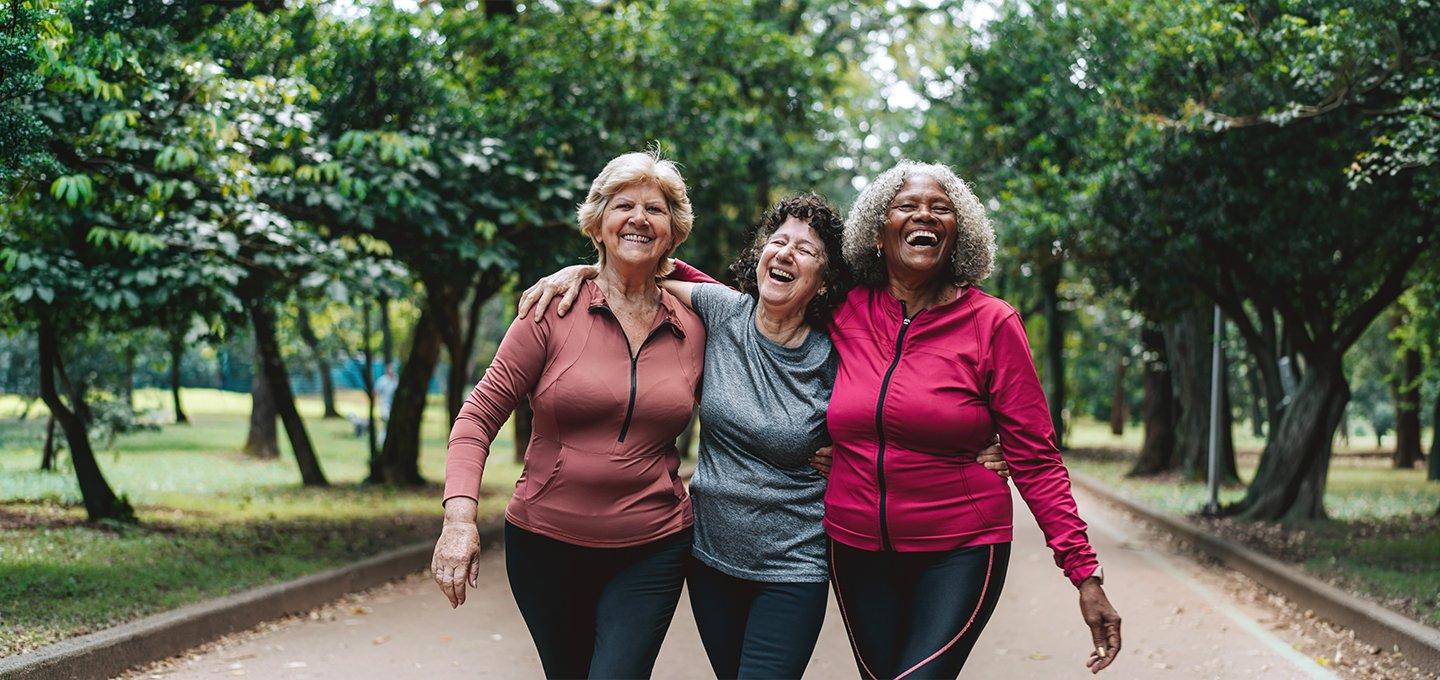 Three people in activewear walking arm in arm in a park.