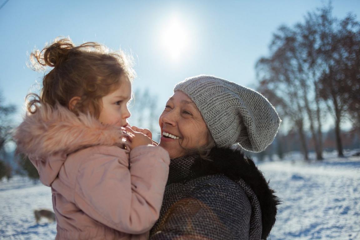 A woman holding a child and smiling outside in the snow